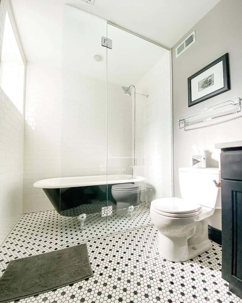 Bright wet room featuring a black-and-white clawfoot tub, glass shower, patterned floor tiles, and a toilet near a towel rack