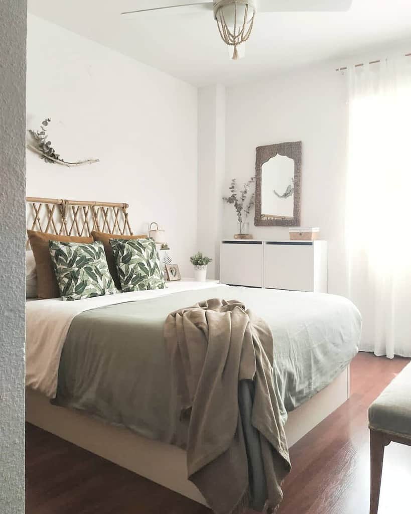 Bright coastal bedroom with a bed, green pillows, and a blanket; natural decor and a white dresser under a window with sheer curtains