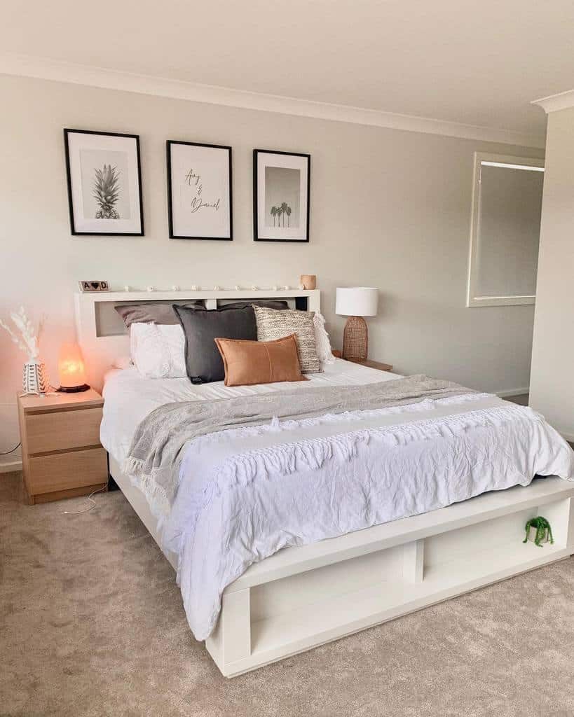 Modern coastal bedroom with neutral tones, framed botanical prints, and a stylish bed frame with built-in storage for a clean, airy feel