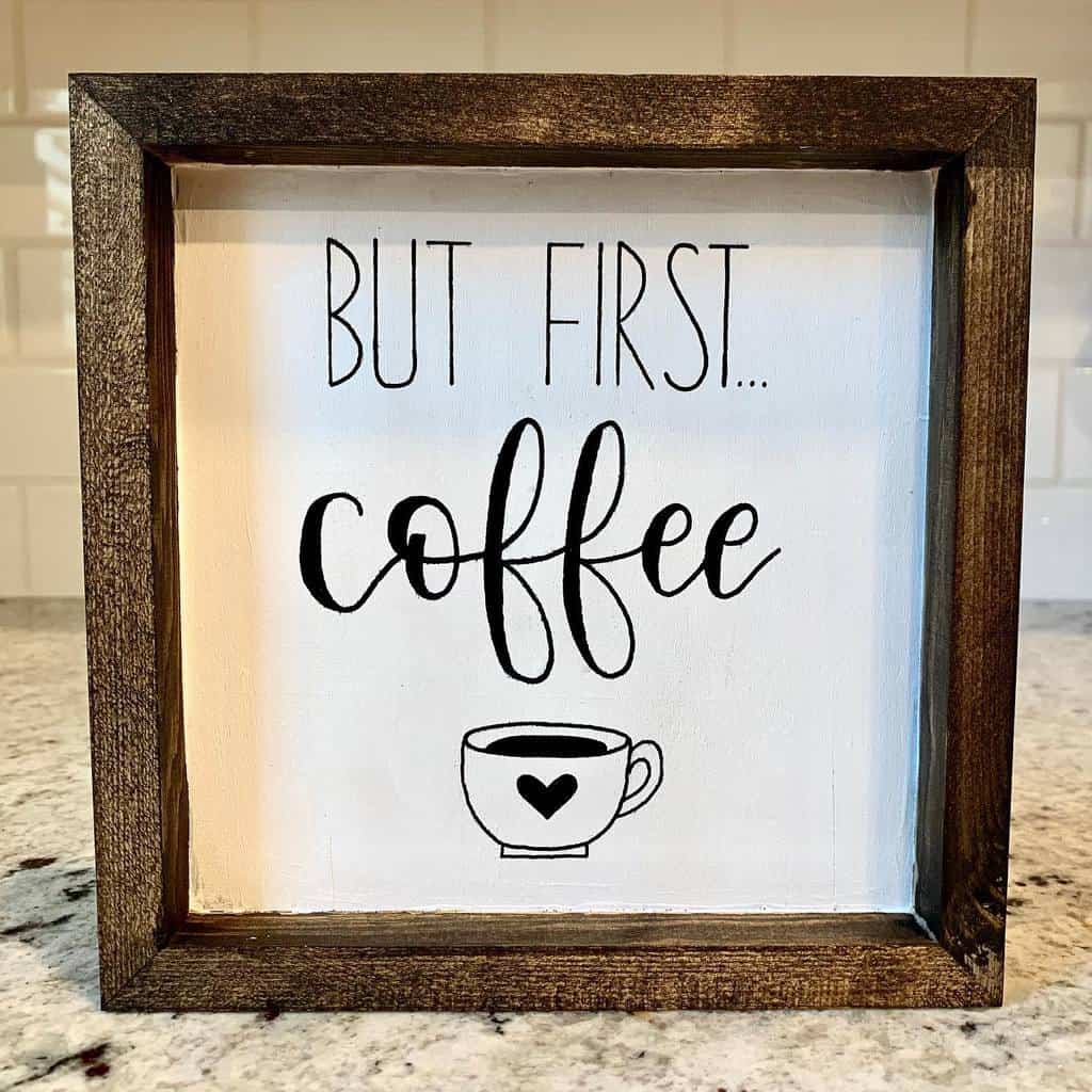 Wood-framed sign on a marble surface reads "But First... Coffee" with a small coffee cup illustration