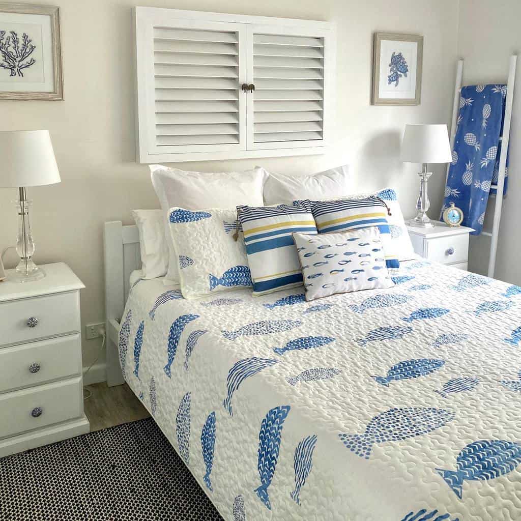 Coastal-themed bedroom with a blue and white fish-patterned quilt, matching pillows, and white furniture and decor