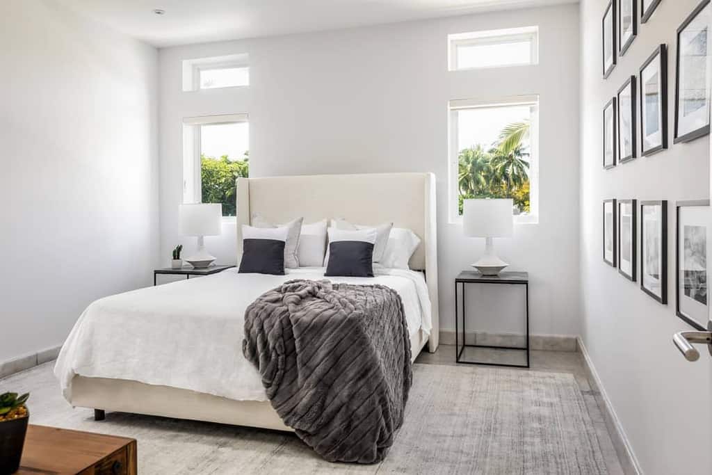 Modern bedroom with white walls, bed with gray blanket, two small bedside tables with lamps, and framed pictures on the wall