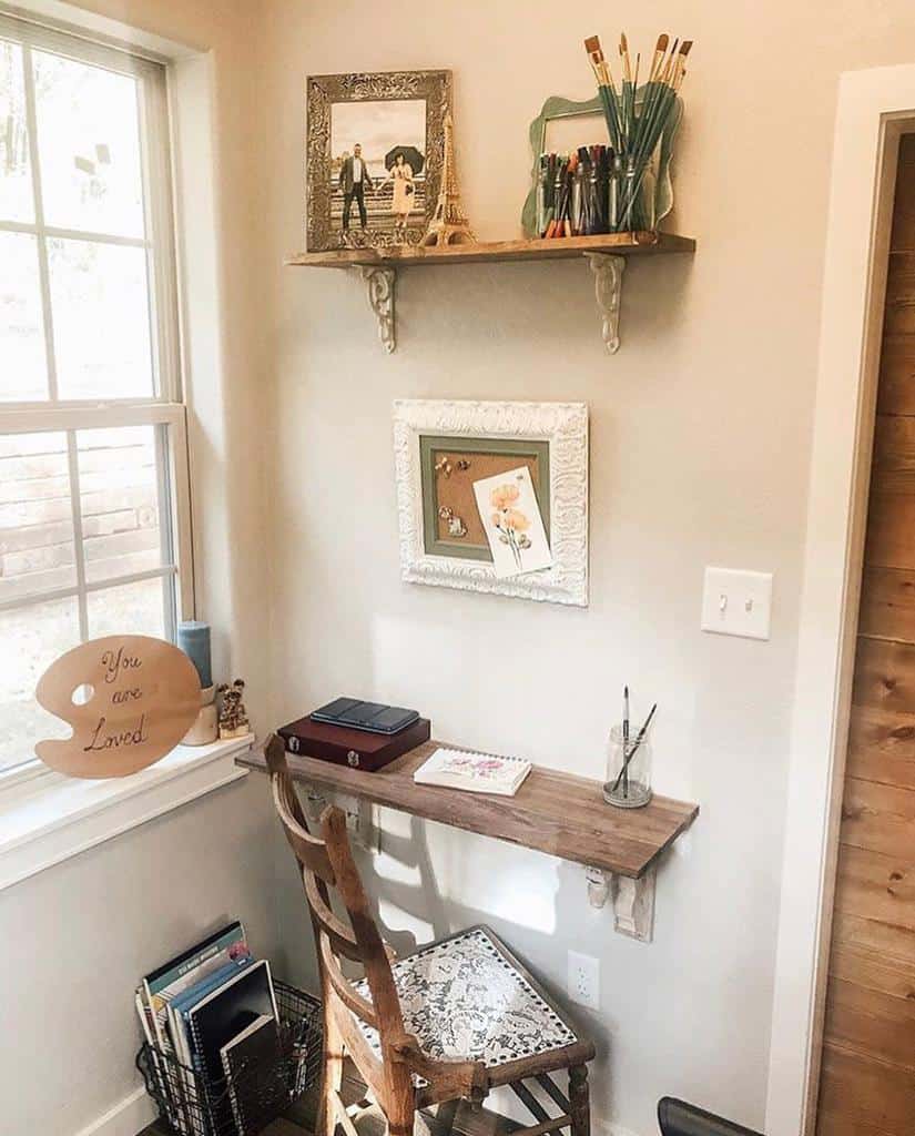 Cozy nook with a wooden desk, chair, art supplies on a shelf, framed photos, and a sign by the window reading "You are Loved"