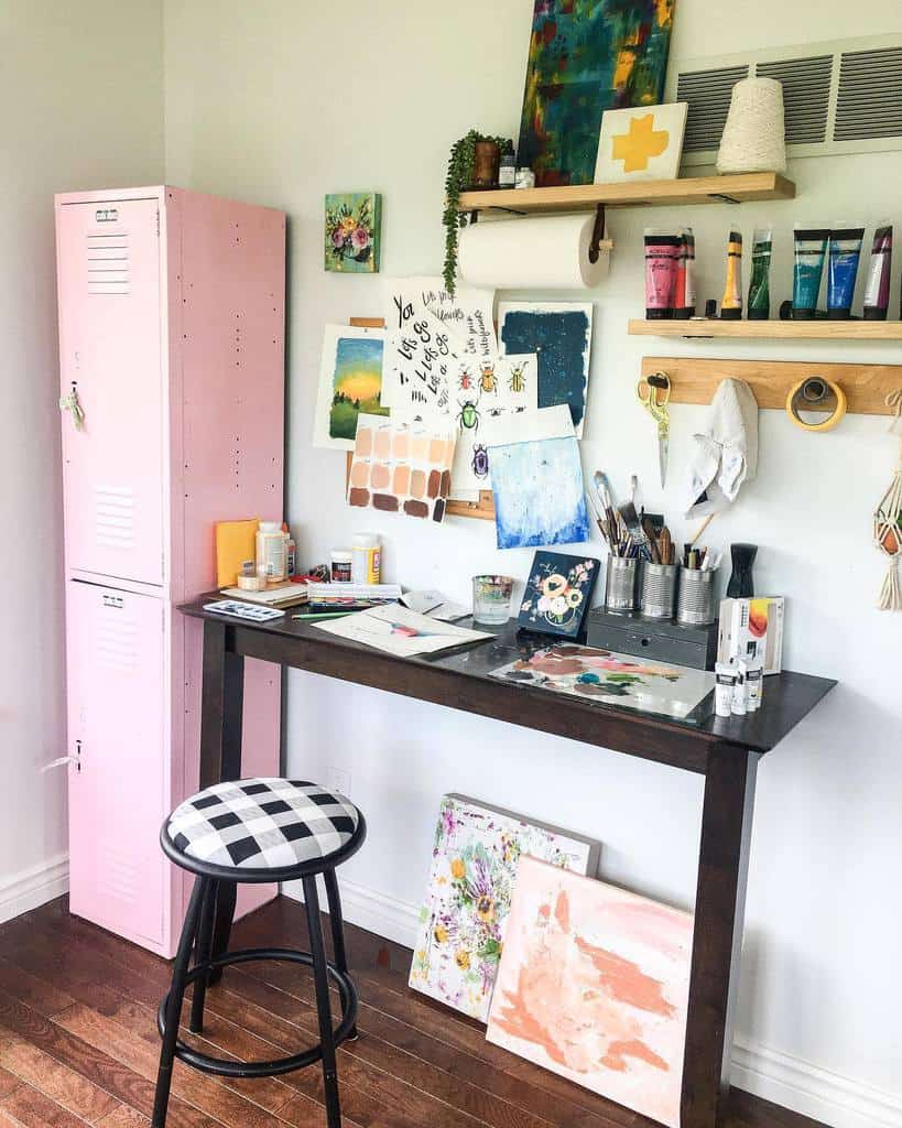 Bright DIY art studio with a wooden desk, pink locker, organized supplies, and colorful paintings on the wall and floor