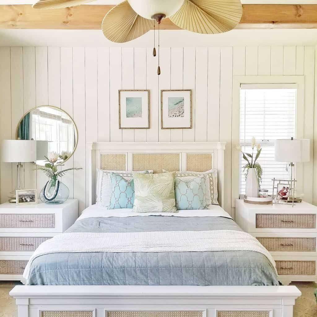 Bright coastal-themed bedroom with a white and beige theme, featuring a made-up bed, two side tables, lamps, a ceiling fan, and decor accents