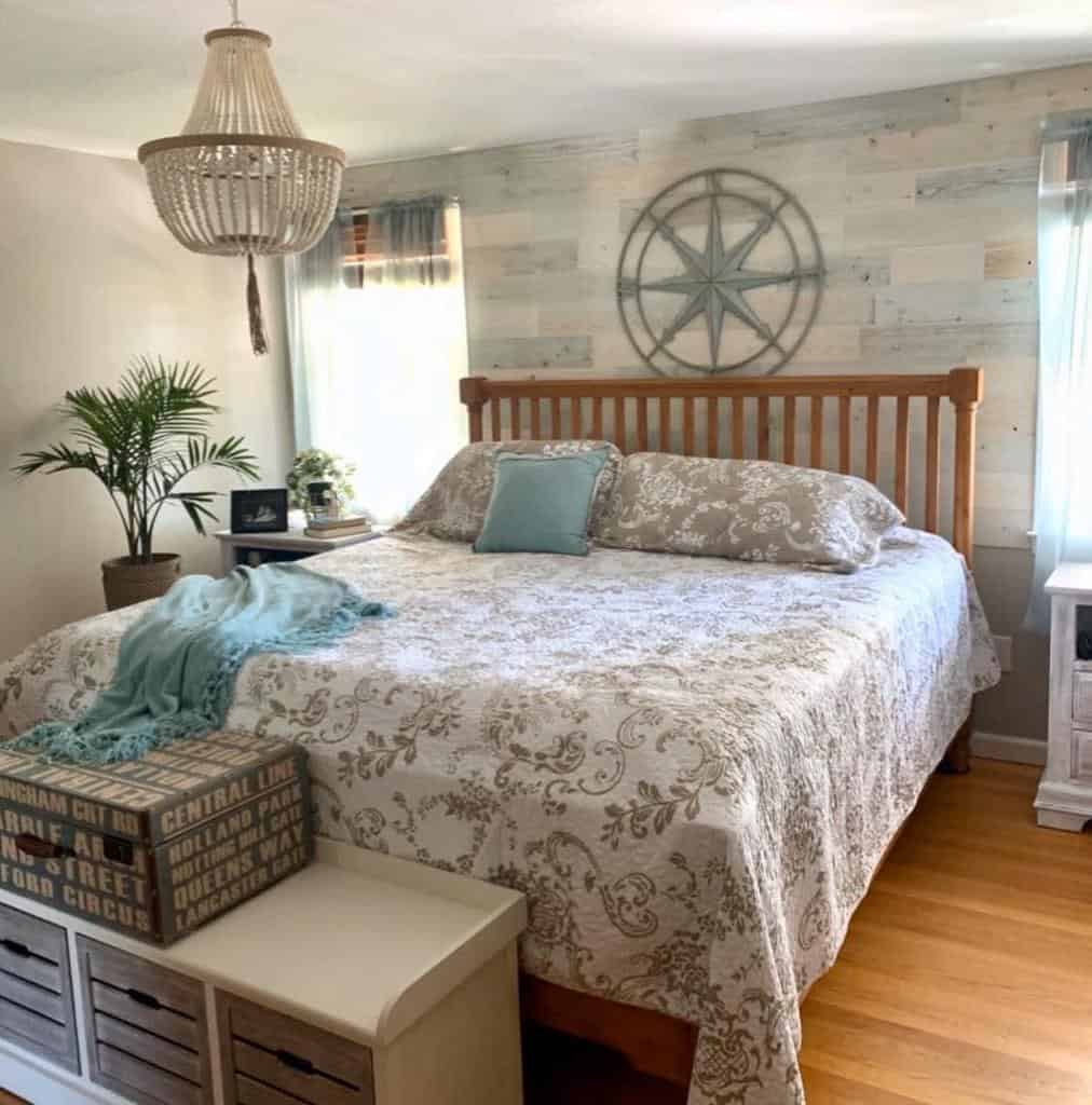 Coastal bedroom with a wooden bed frame, nautical wall decor, and soft blue accents, featuring a rustic chandelier and airy textures