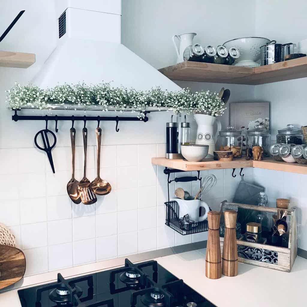 A cozy kitchen corner with wooden shelves, copper utensils, spice jars, and a white range hood adorned with flowers