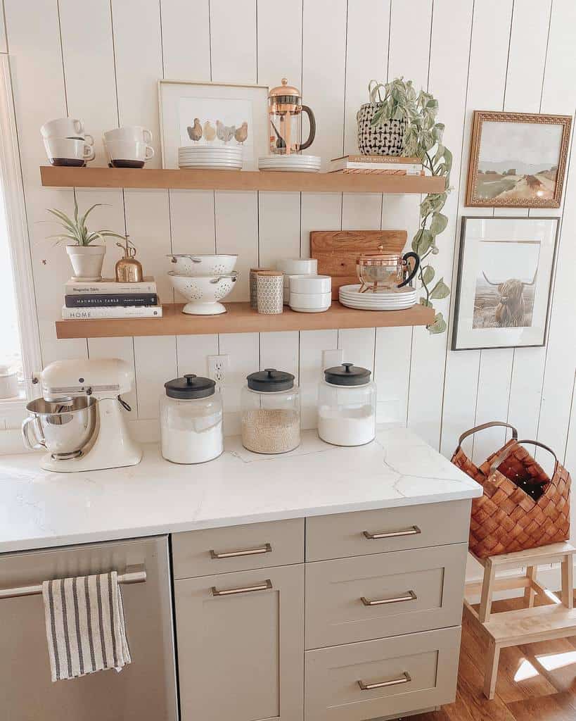 Minimalist wooden shelves on a white shiplap wall display neutral-toned dishes, books, and plants, creating a cozy farmhouse kitchen look