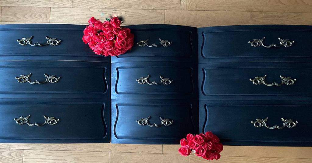 Elegant black chalk-painted dresser drawers with ornate gold handles, styled with vibrant red roses on a wooden floor