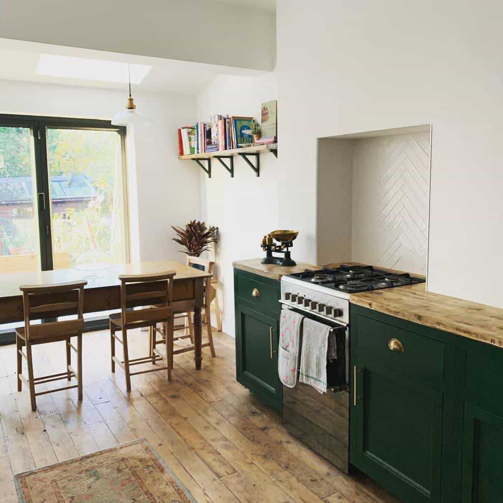 Bright kitchen with dark green chalk-painted cabinets, wooden countertops, a farmhouse dining table, and natural light from glass doors