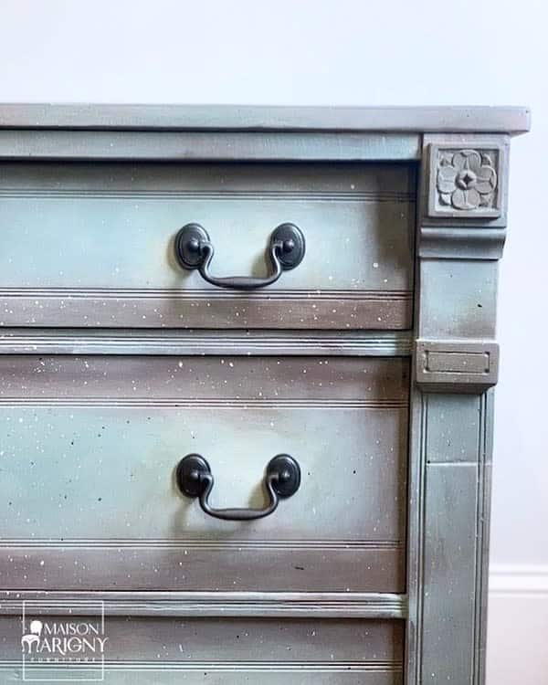 Vintage dresser with a weathered blue-gray chalk paint finish, black metal handles, and floral wood detailing on the corner post