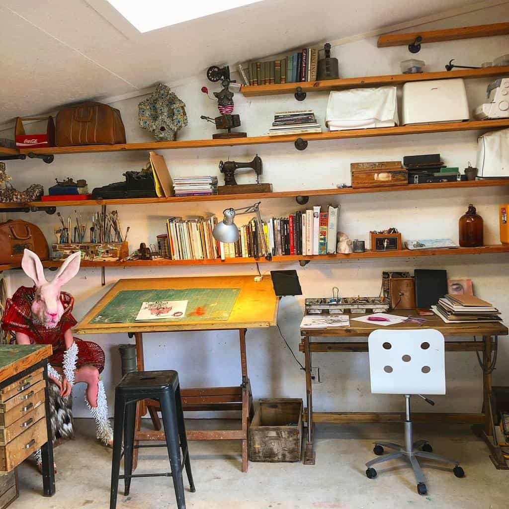 Eclectic art studio with wooden shelves, vintage decor, drafting desks, and a person in a surreal rabbit mask and costume