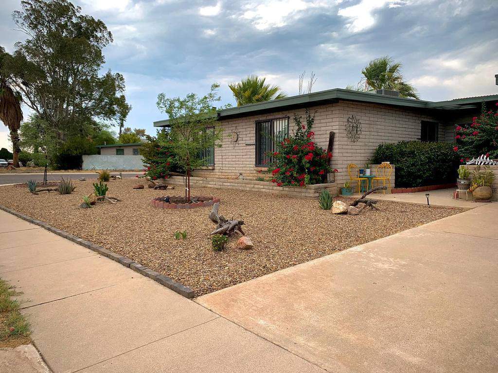 Front yard xeriscape with gravel, drought-tolerant plants, and flowering bushes surrounding a brick house under a cloudy sky