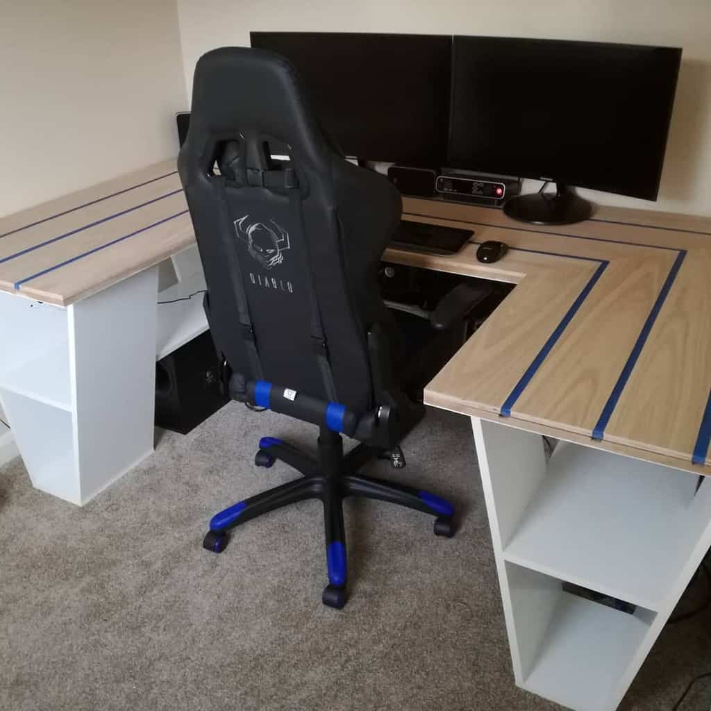 L-shaped desk with blue accents, gaming chair, dual monitors, and organized shelves, set up on carpeted floor