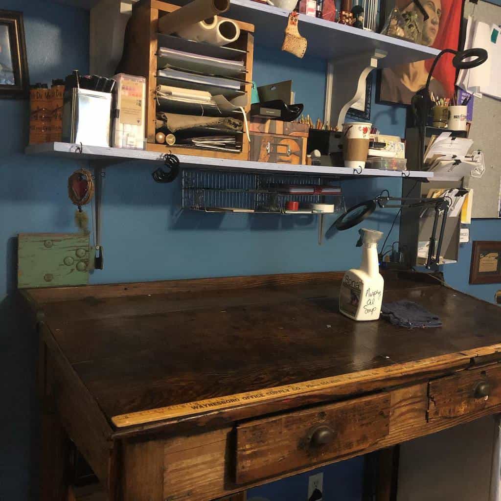 Rustic art studio workspace with a wooden desk, blue walls, open shelves filled with supplies, and organized tools for creativity