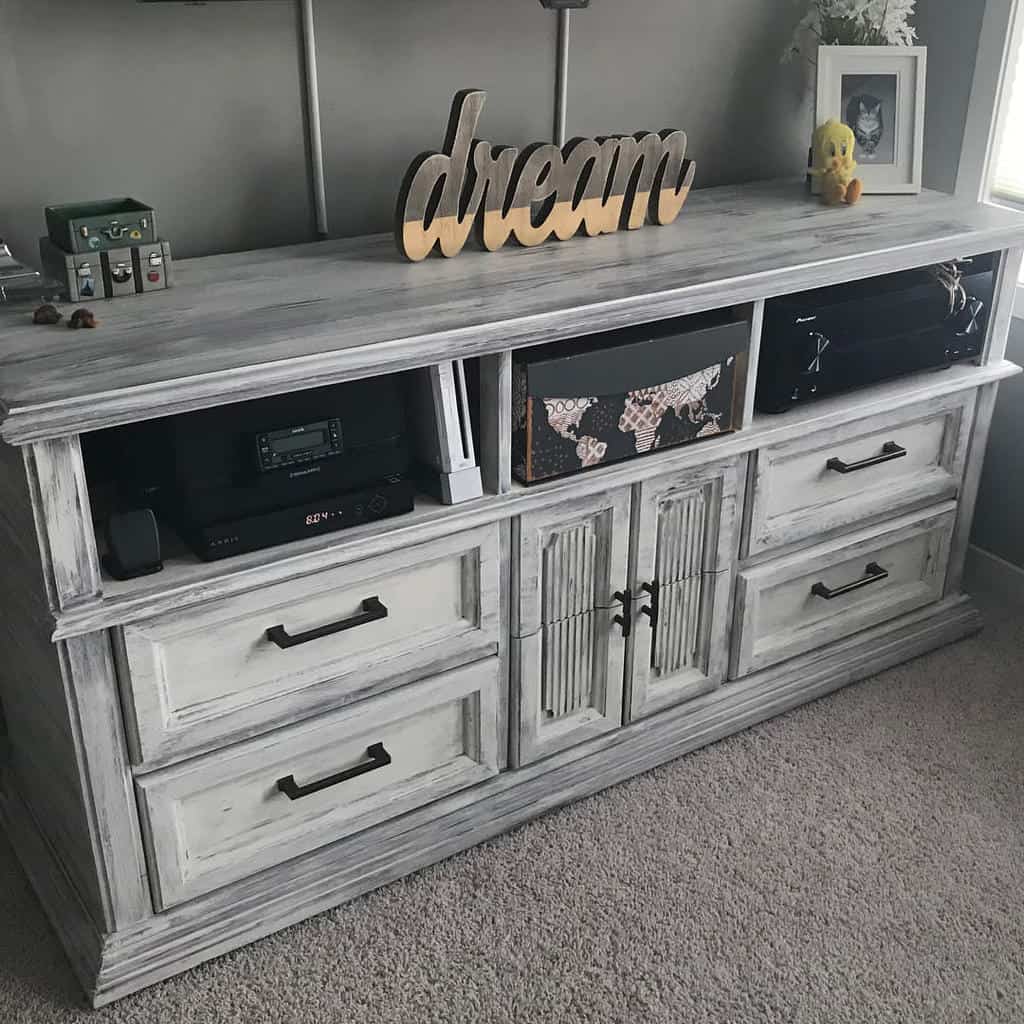 Distressed white and gray chalk-painted media console with black handles, open shelving, and a 'dream' wooden sign on top