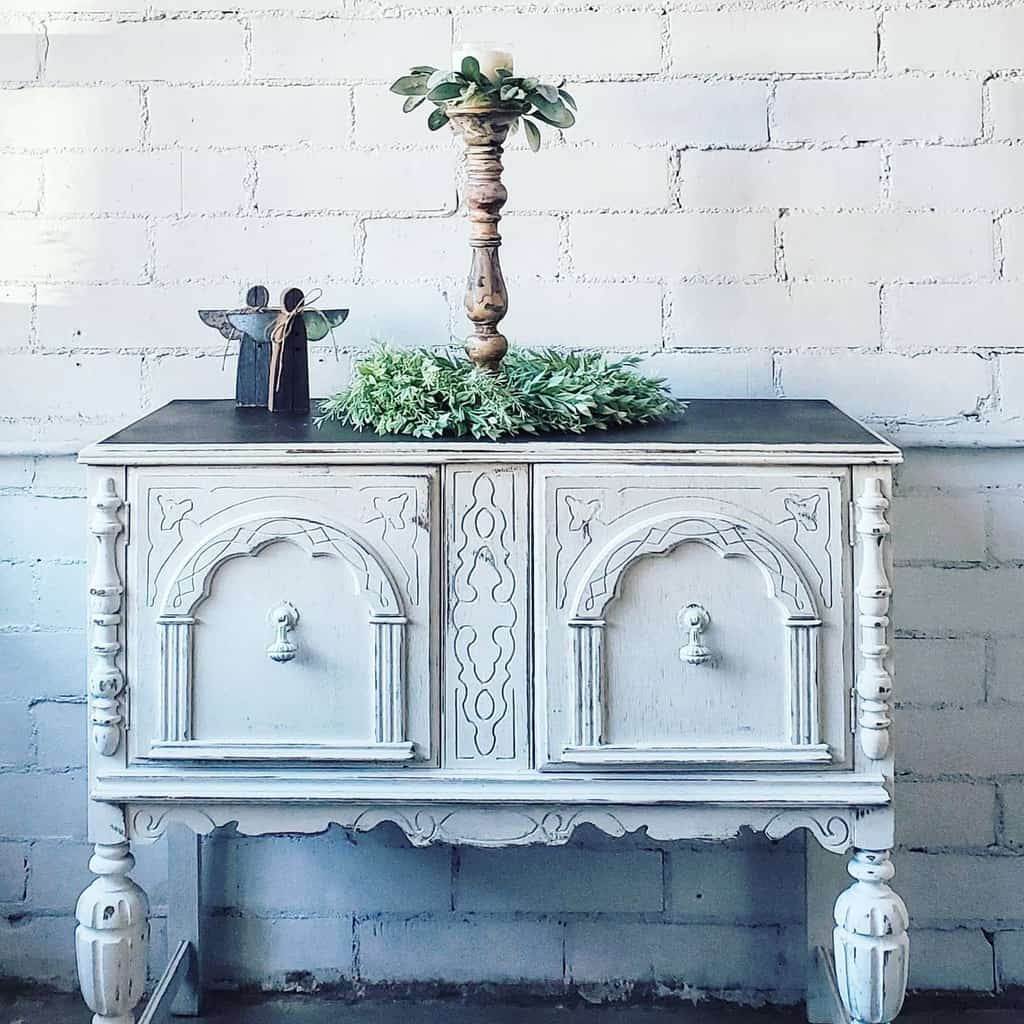 Vintage sideboard with a distressed white chalk paint finish, ornate details, and a dark top, styled with rustic holiday decor