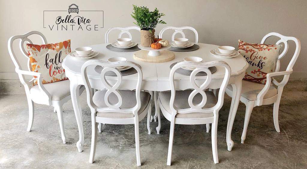 White chalk-painted vintage dining set with elegant chairs, fall-themed pillows, and a cozy tablescape featuring pumpkins and greenery