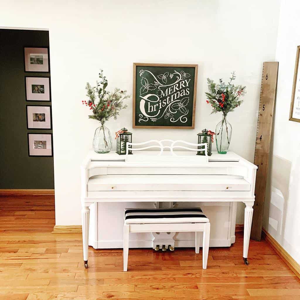 White chalk-painted piano with a matching bench, decorated with Christmas greenery, lanterns, and a festive 'Merry Christmas' chalkboard sign