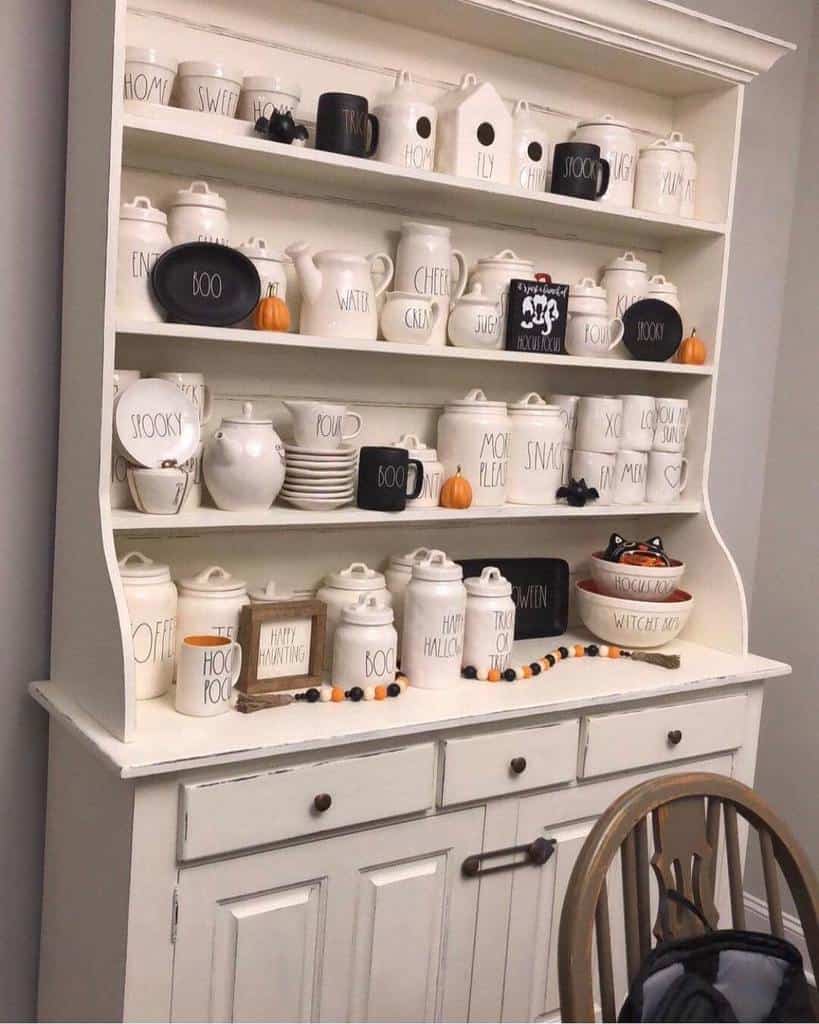 White chalk-painted farmhouse hutch decorated with Rae Dunn pottery, Halloween-themed accents, and rustic fall decor