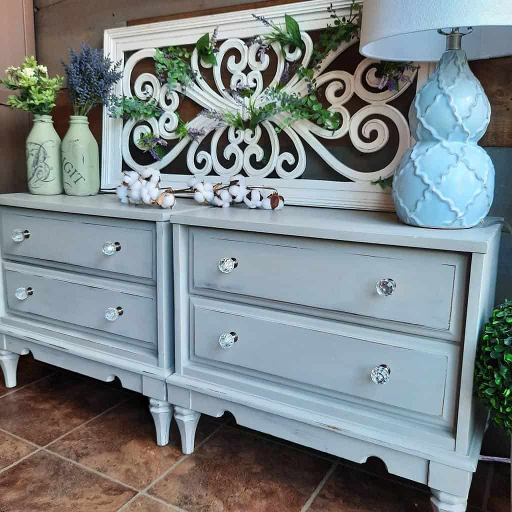 Light gray chalk-painted farmhouse dressers with glass knobs, decorated with rustic greenery, cotton stems, and a blue textured lamp