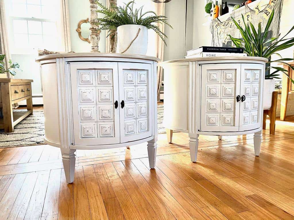 Pair of white chalk-painted farmhouse side tables with intricate panel detailing, styled with greenery in a bright, cozy living space