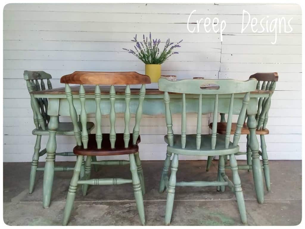 Rustic farmhouse dining set with sage green chalk-painted chairs and a wooden tabletop, styled with a lavender centerpiece against a white backdrop