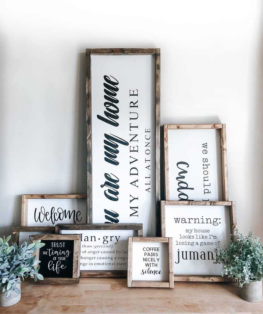 Decorative wooden-framed signs with quotes, arranged on a table, surrounded by small potted plants