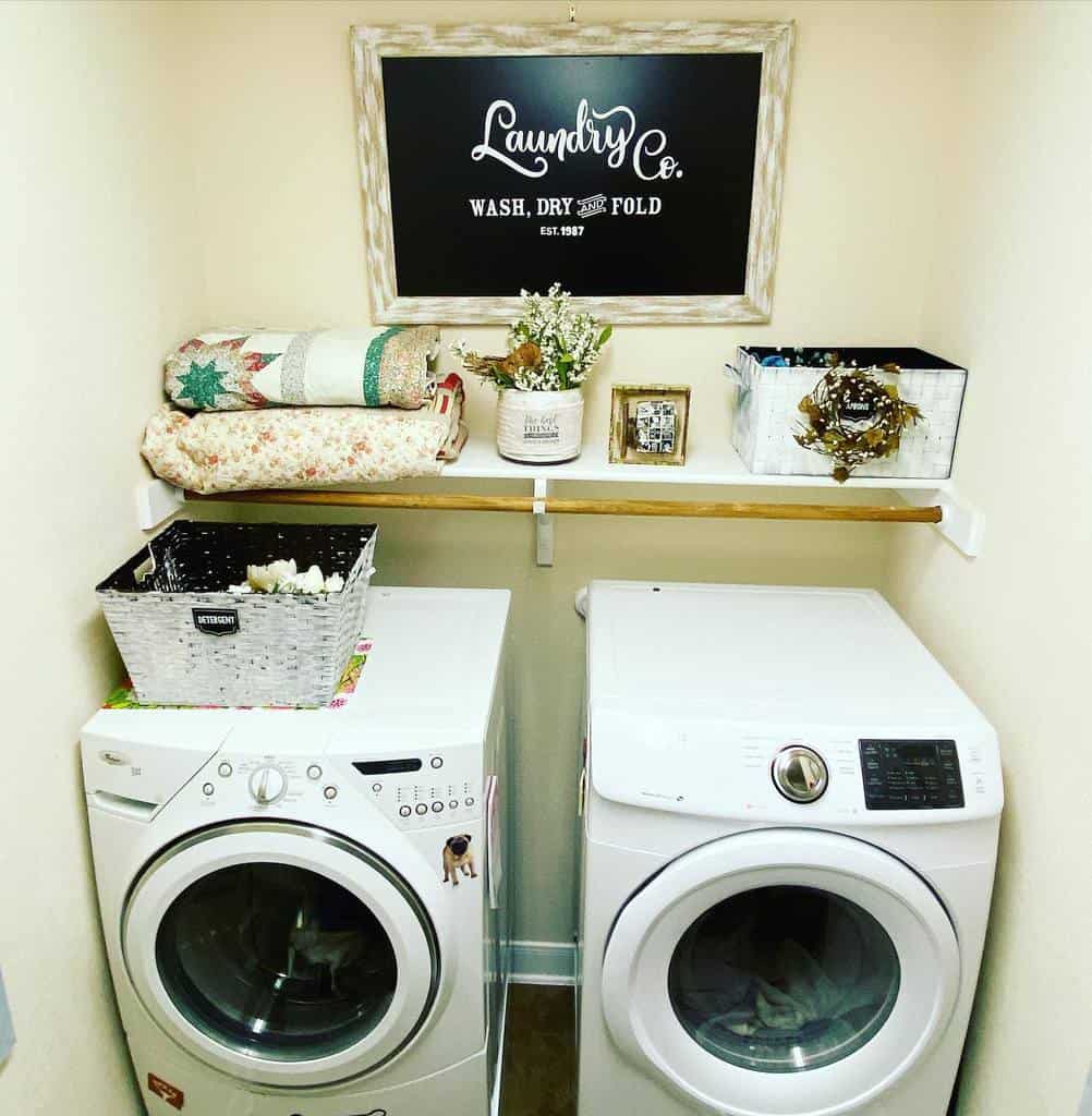 Cozy laundry room with a farmhouse-style 'Laundry Co. Wash, Dry, Fold' wood sign, vintage quilts, and rustic decor on a wall shelf