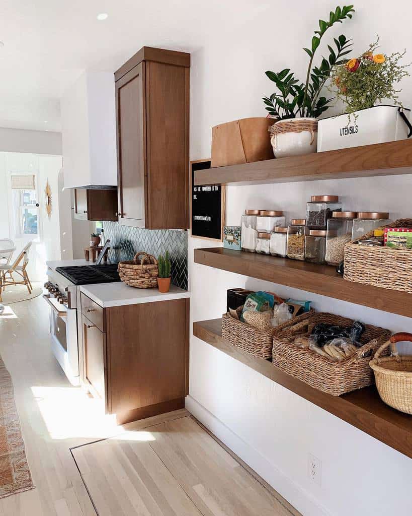 Modern kitchen with wooden cabinets, open floating shelves with jars, baskets, and plants, green chevron backsplash and light wood flooring