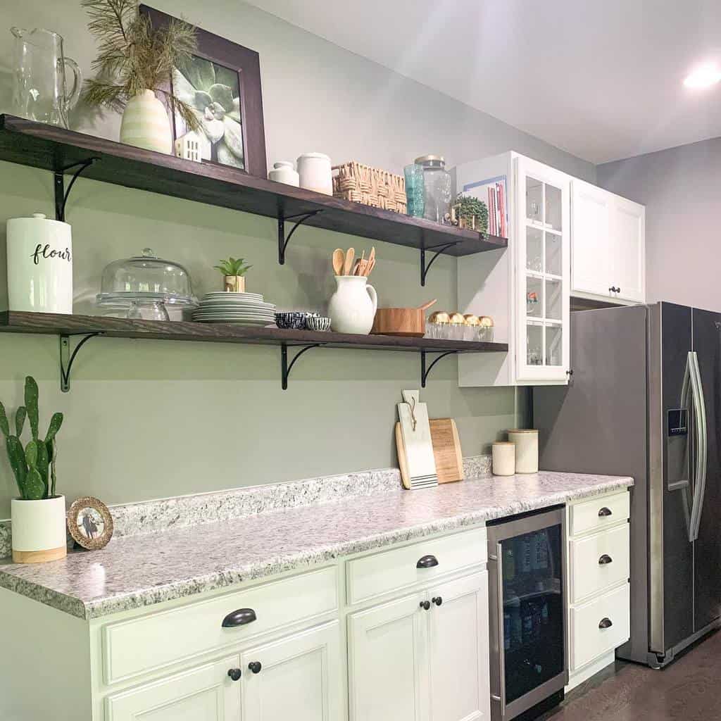 Modern kitchen with white cabinets, open wooden shelves, and a gray countertop decorated with plants, dishes, and jars