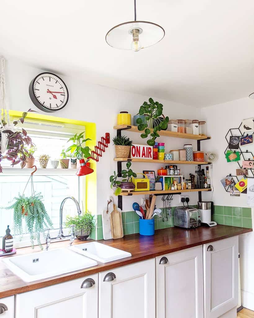 Bright kitchen with plants, wall floating shelves holding jars and decor, clock, and "ON AIR" sign above sink with green tiles