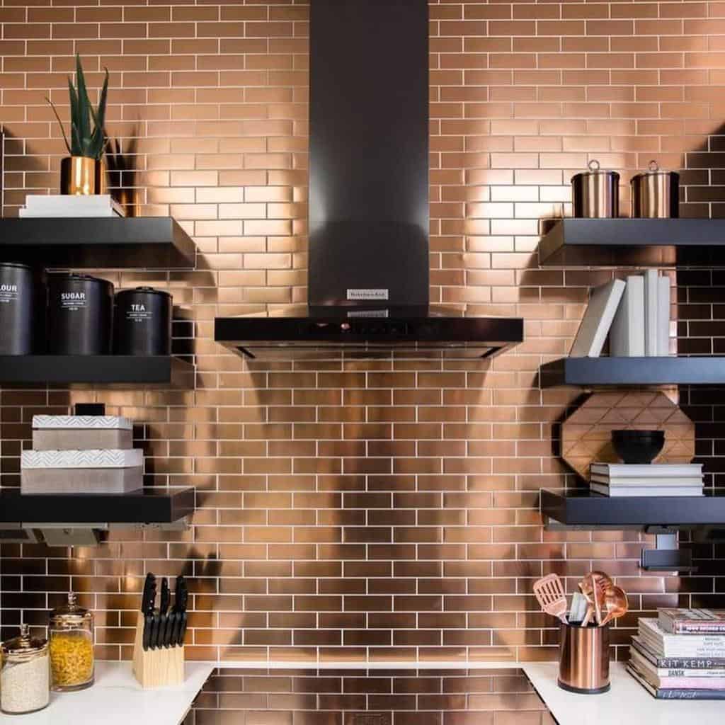 Modern kitchen with copper backsplash, black floating shelves, cookware, and utensils; white countertop with knife set and jars