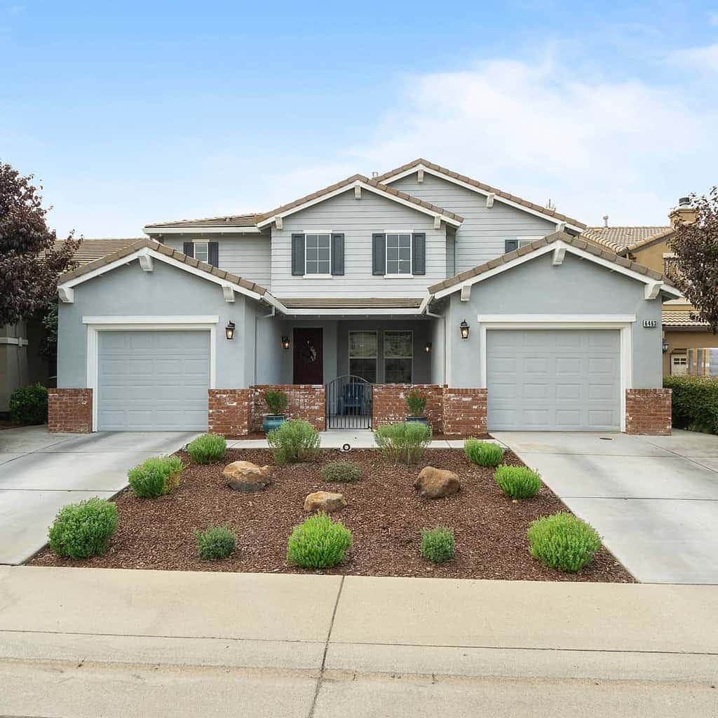 Modern front yard xeriscape with drought-tolerant plants, mulch, and decorative rocks in front of a two-story suburban home