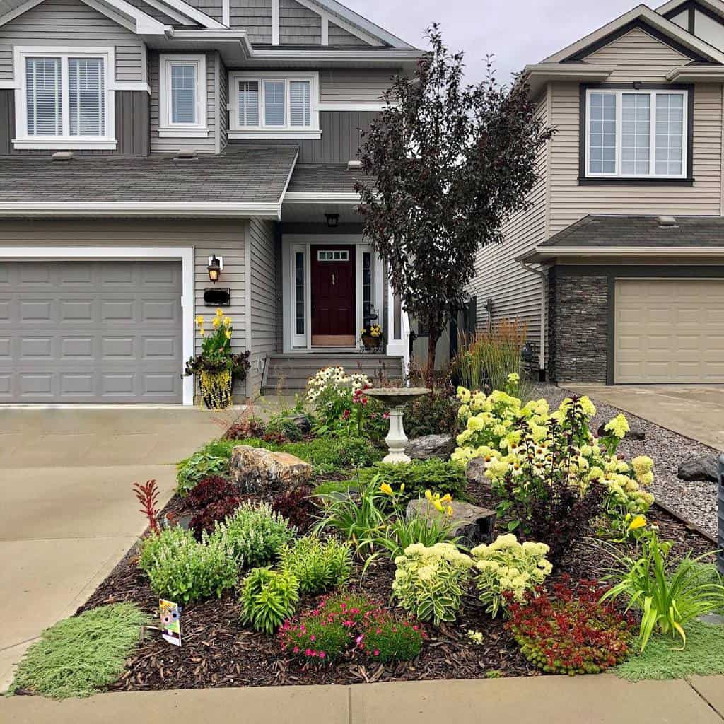 Beautiful front yard xeriscape with lush drought-tolerant plants, mulch, a bird bath, and decorative rocks in front of a modern home