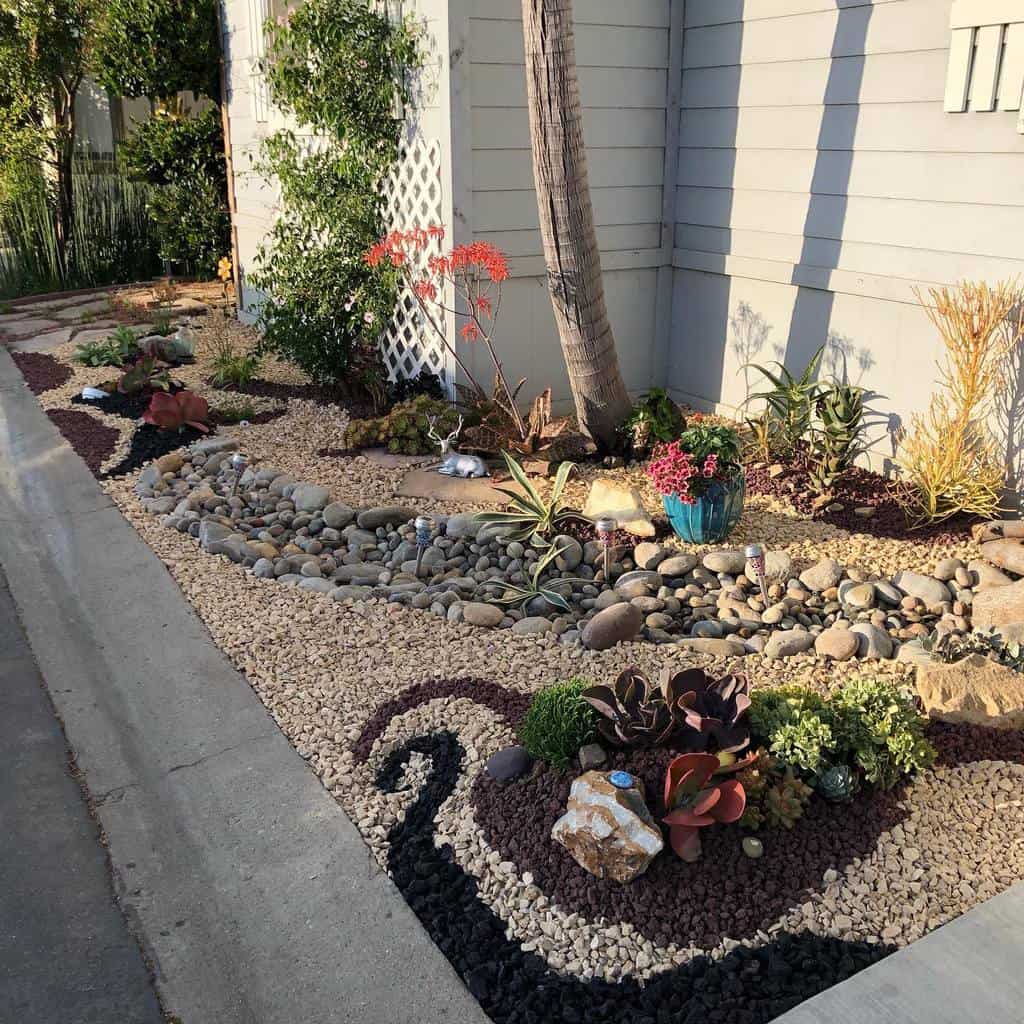 Creative front yard xeriscape design with decorative gravel patterns, drought-tolerant plants, succulents, a dry riverbed, and a palm tree against a house exterior