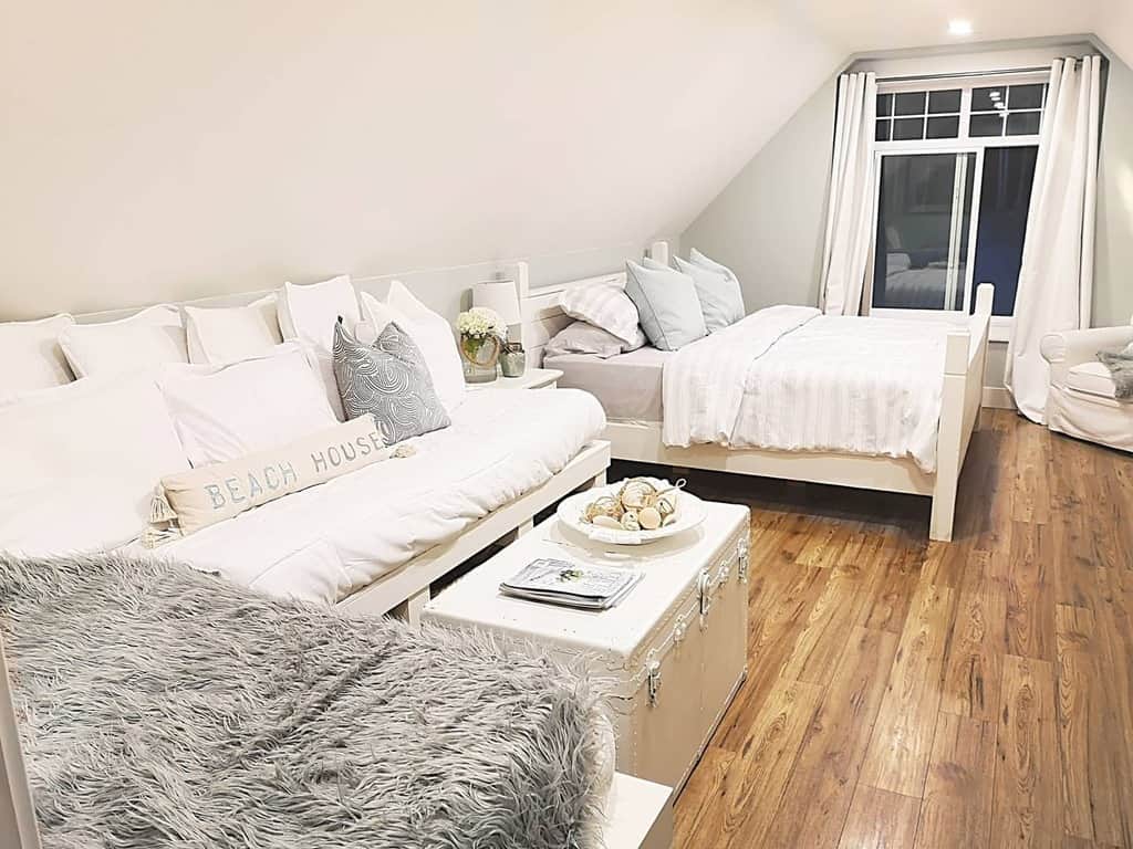 Bright coastal bedroom with white wooden furniture, soft neutral bedding, and beach-inspired decor, creating a cozy and airy retreat