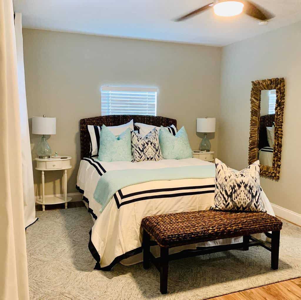 Cozy bedroom with a neatly made bed, light blue and white linens, two nightstands with lamps, a decorative mirror, and a ceiling fan