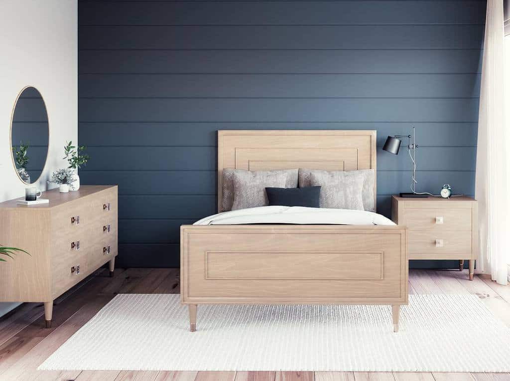 Minimalist bedroom with a wood bed, dresser, nightstand, gray accent wall, round mirror, white rug, and a lamp immersed in bright natural light