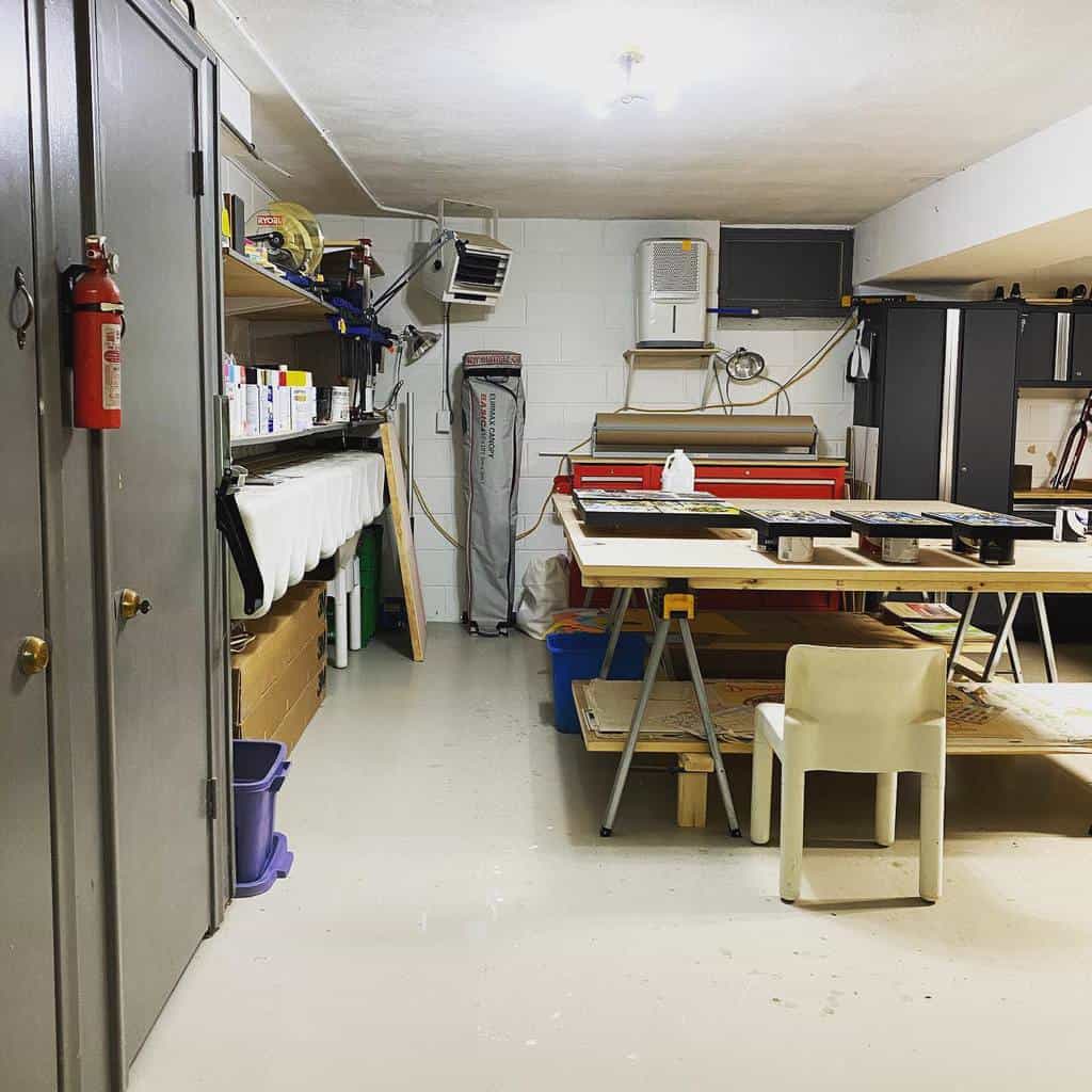 Spacious garage art studio with work tables, organized storage, shelves with supplies, and industrial equipment for creative projects