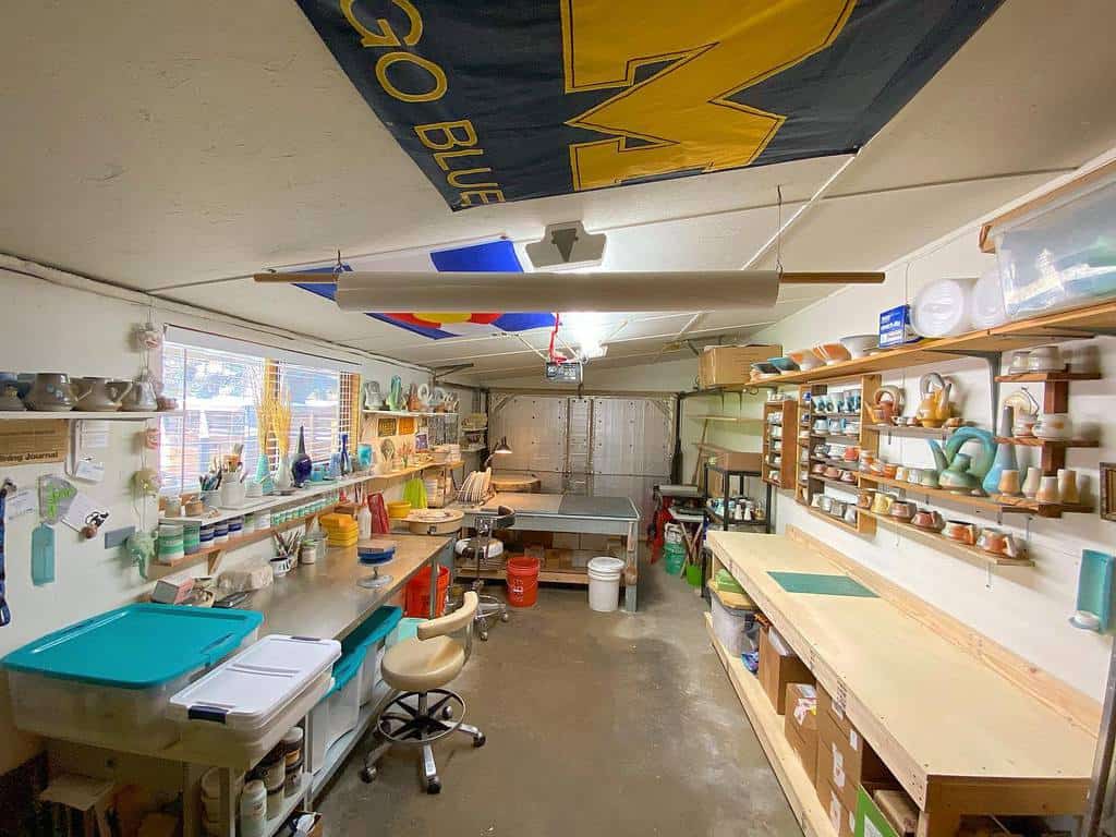 A pottery studio with shelves of ceramics, a workbench, tools, and a "GO BLUE" banner hanging from the ceiling