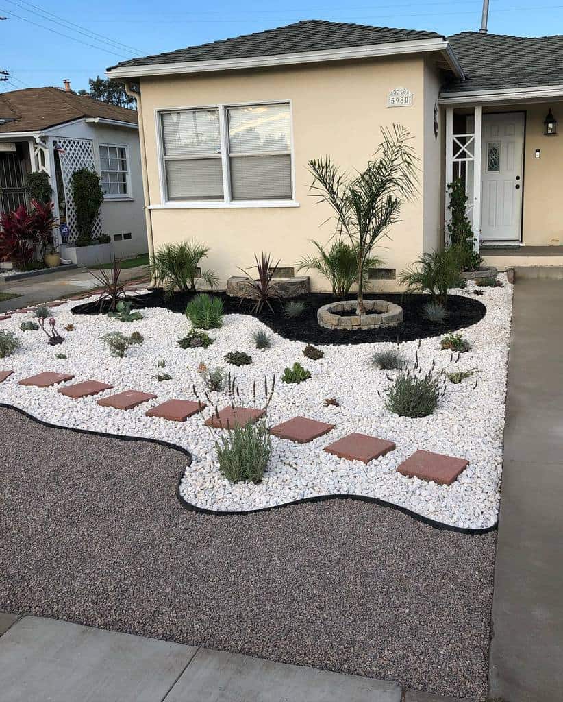 Modern xeriscape front yard with white gravel, drought-tolerant plants, a palm tree, and a red stepping stone path