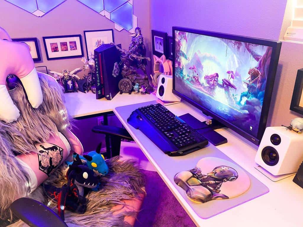 Cozy gaming setup with a colorful monitor display, themed accessories, plush toys on chair, and ambient lighting