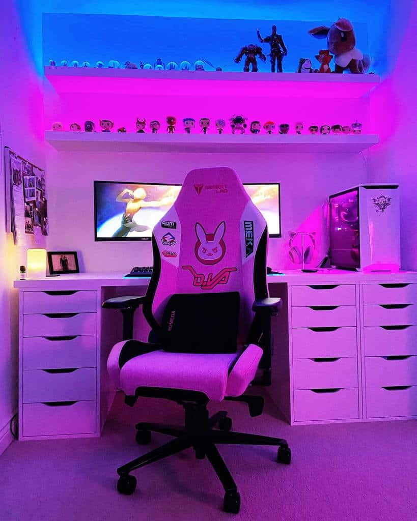 Gaming setup with a pink and white chair, dual monitors, neon lights, and shelves displaying action figures, creating a cozy and colorful ambiance