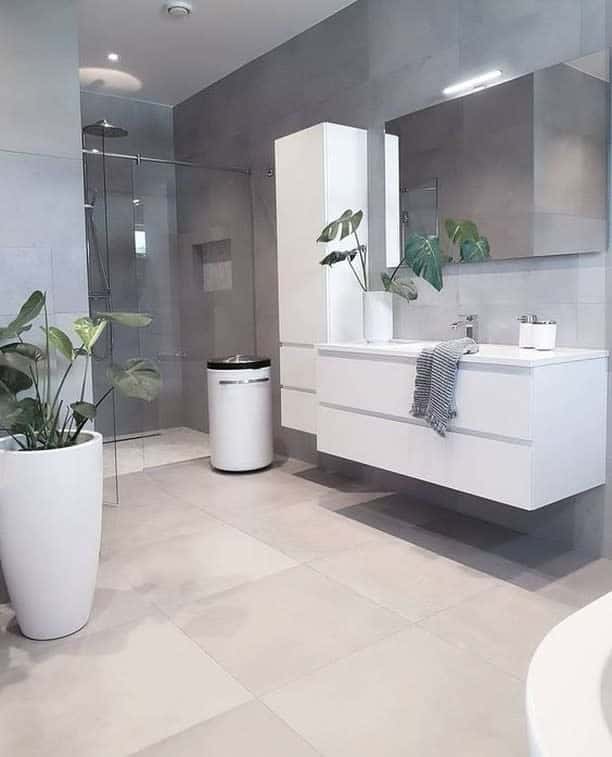 Modern wet room with large tiles, glass shower, white vanity, and potted plants; minimalist decor with neutral tones