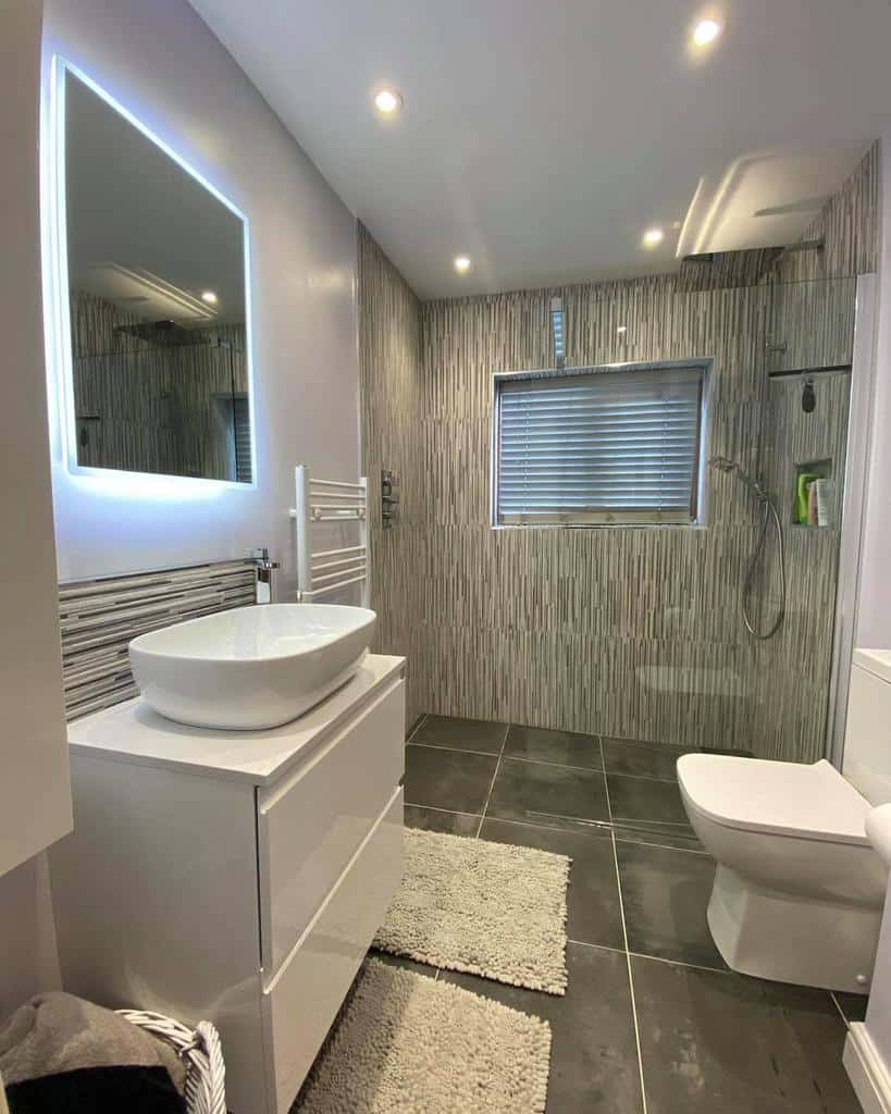 Modern wet room with sleek grey tiles, LED mirror, vessel sink, and walk-in shower, creating a stylish and functional space