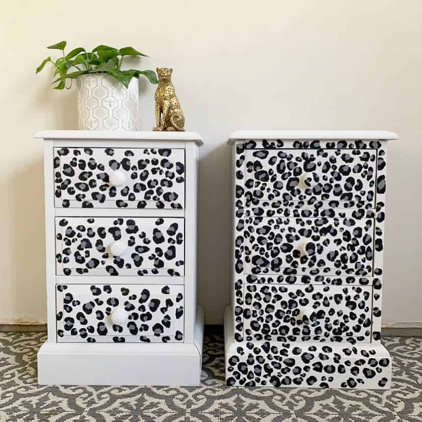 White chalk-painted nightstands with hand-painted black leopard print drawers, styled with a gold cheetah figurine and a potted plant