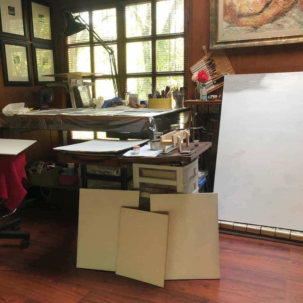 Artist's studio with blank canvases, a desk with art supplies, and a large window letting in natural light