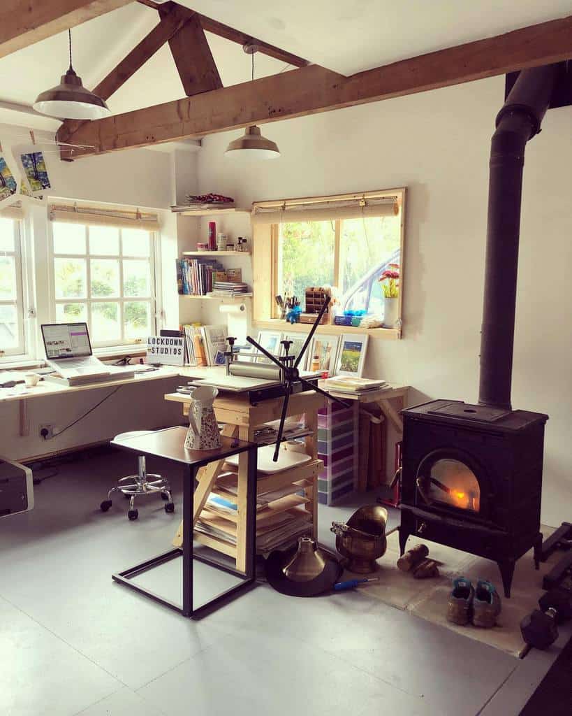 Cozy home office with a wood-burning stove, shelves, desk with a computer, and natural light from large windows