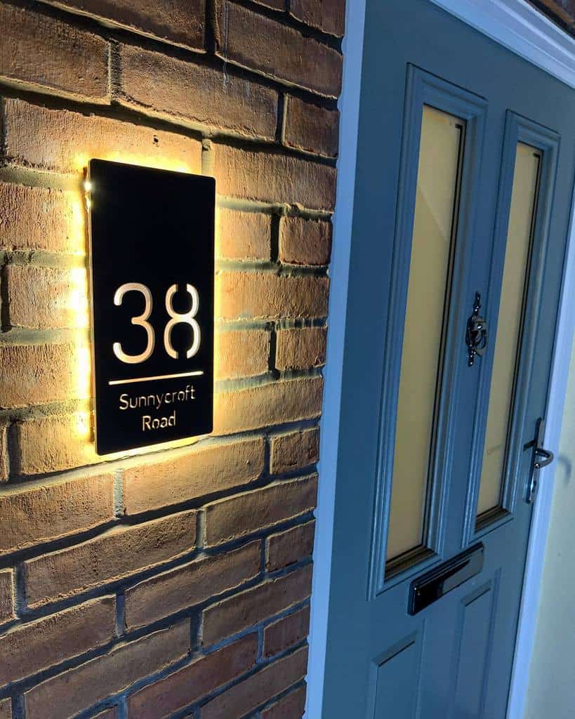 Illuminated house sign displaying "38 Sunnycroft Road" on a brick wall by the blue door